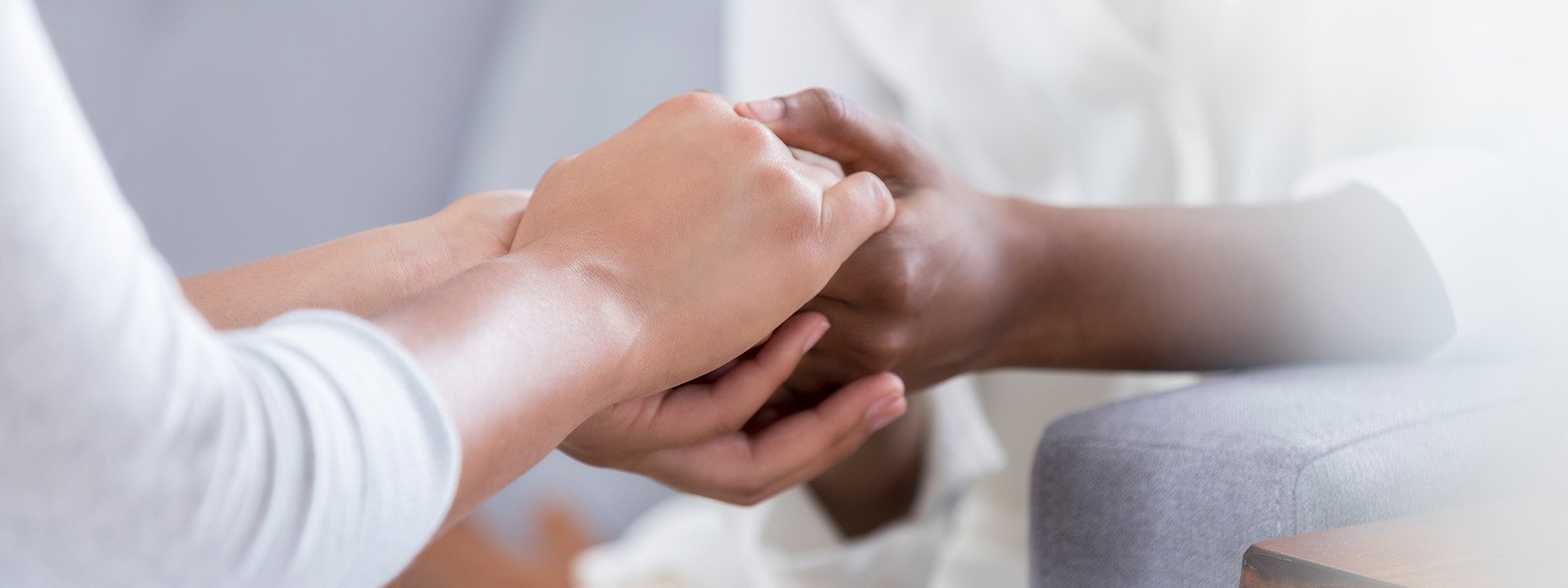 Female friends hold hands together as they pray or comfort one another