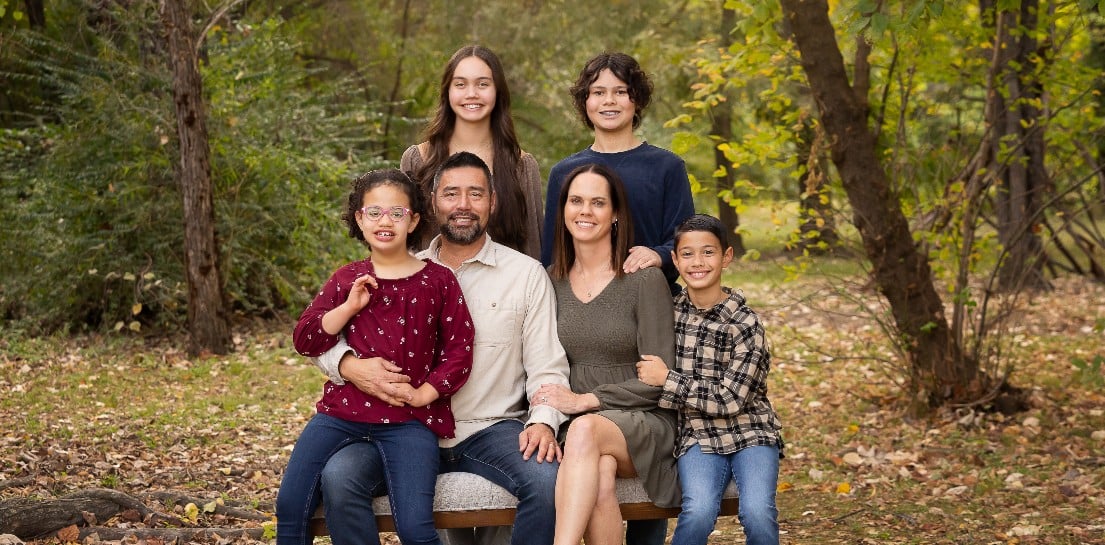 A family of six sits outside for a picture. There are two parents, and four kids