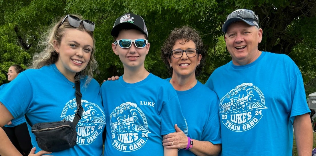 A family of four stands outside for a picture. There are two parents, and two older kids