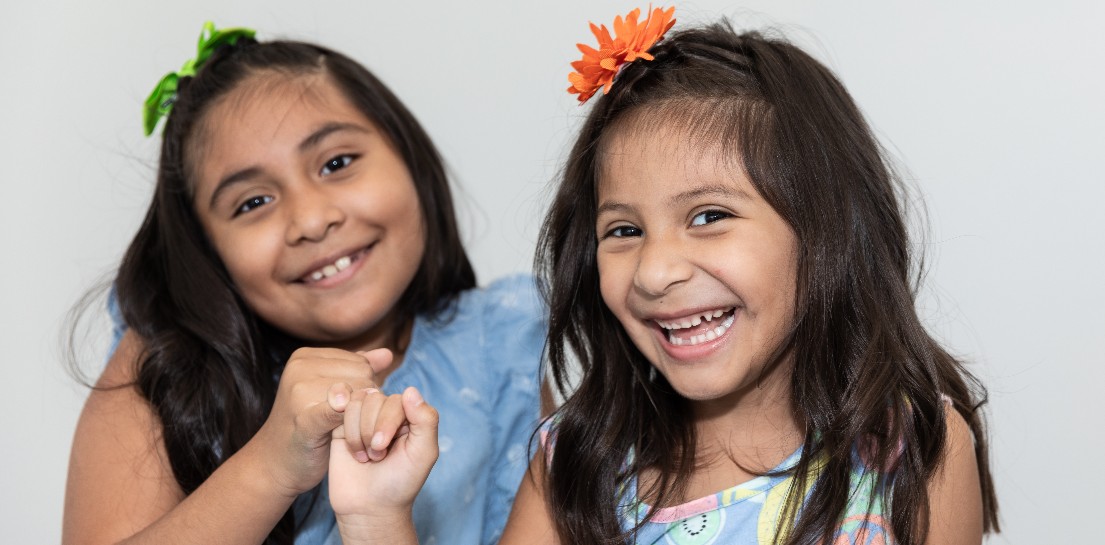 Two young girls smiling with colorful flowers in their hair