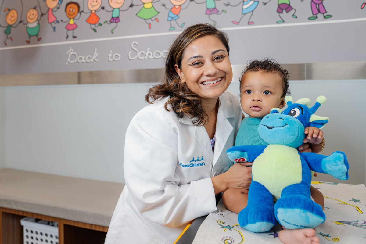 Pediatric physician holding a baby after a wellness check at a pediatric primary care office in Plano, Texas