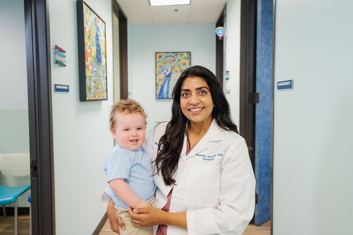 Pediatric physician smiling and holding a baby after a health check at a pediatric primary care office in Plano, Texas