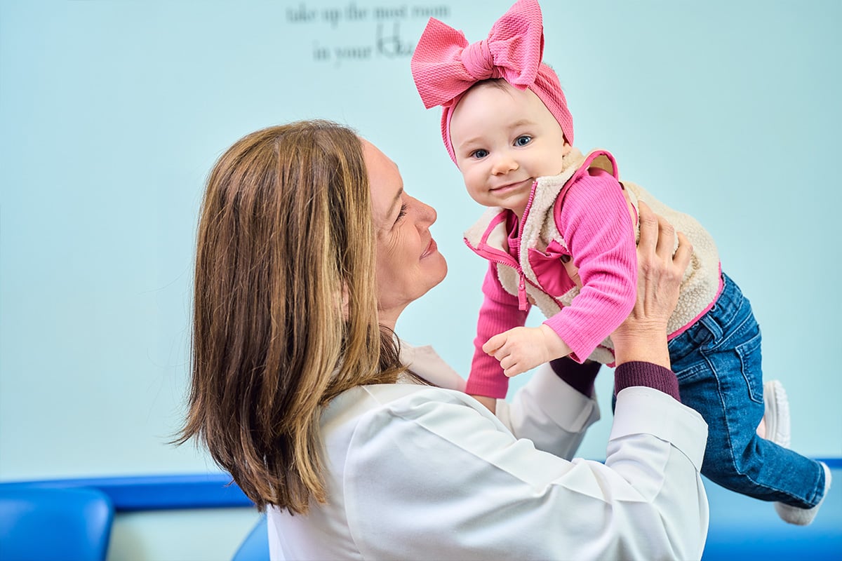 A pediatrician in Plano carrying a baby wearing a pink bow