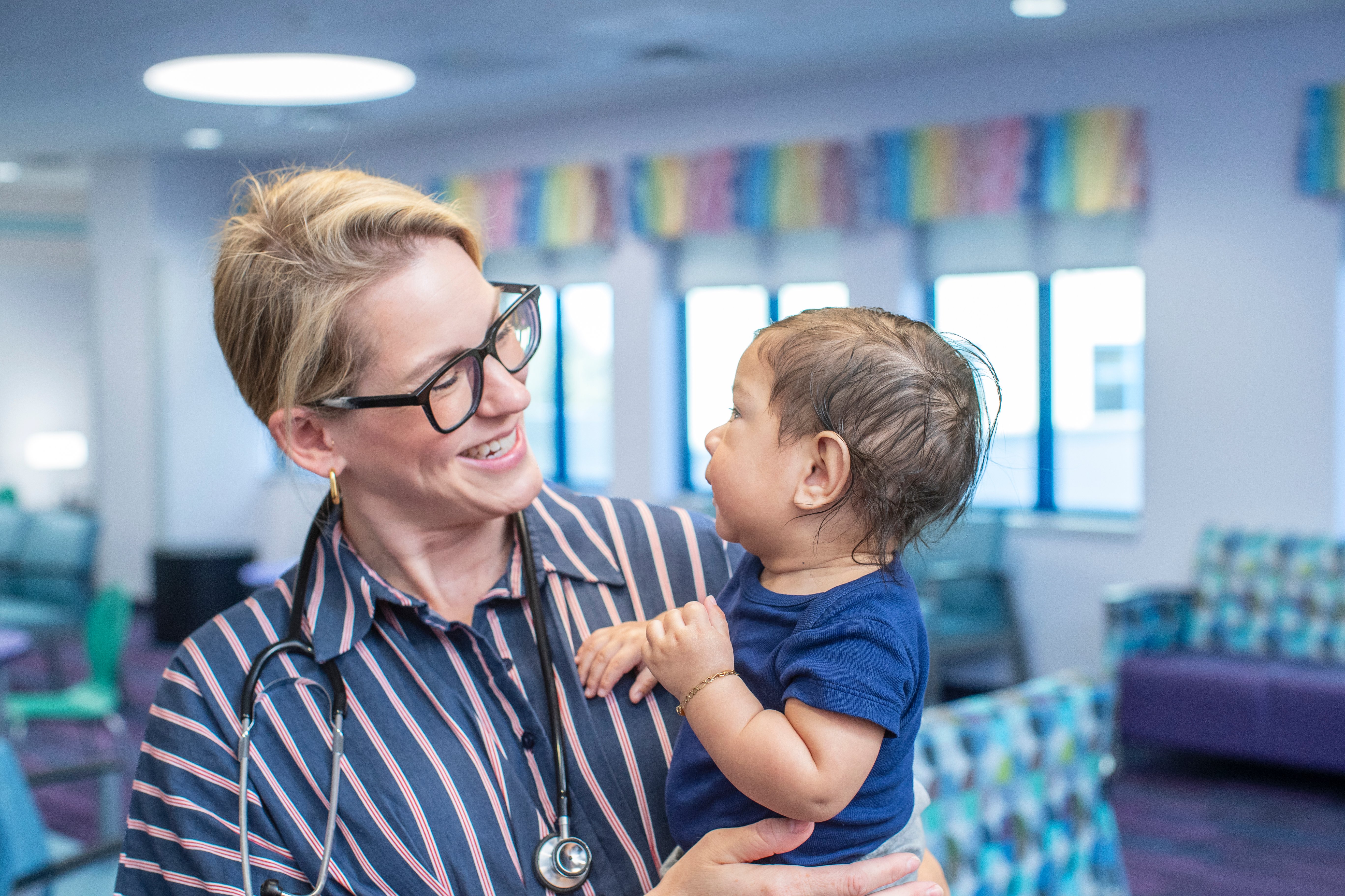 Pediatric surgeon and baby smiling at eachother in a clinic lobby.