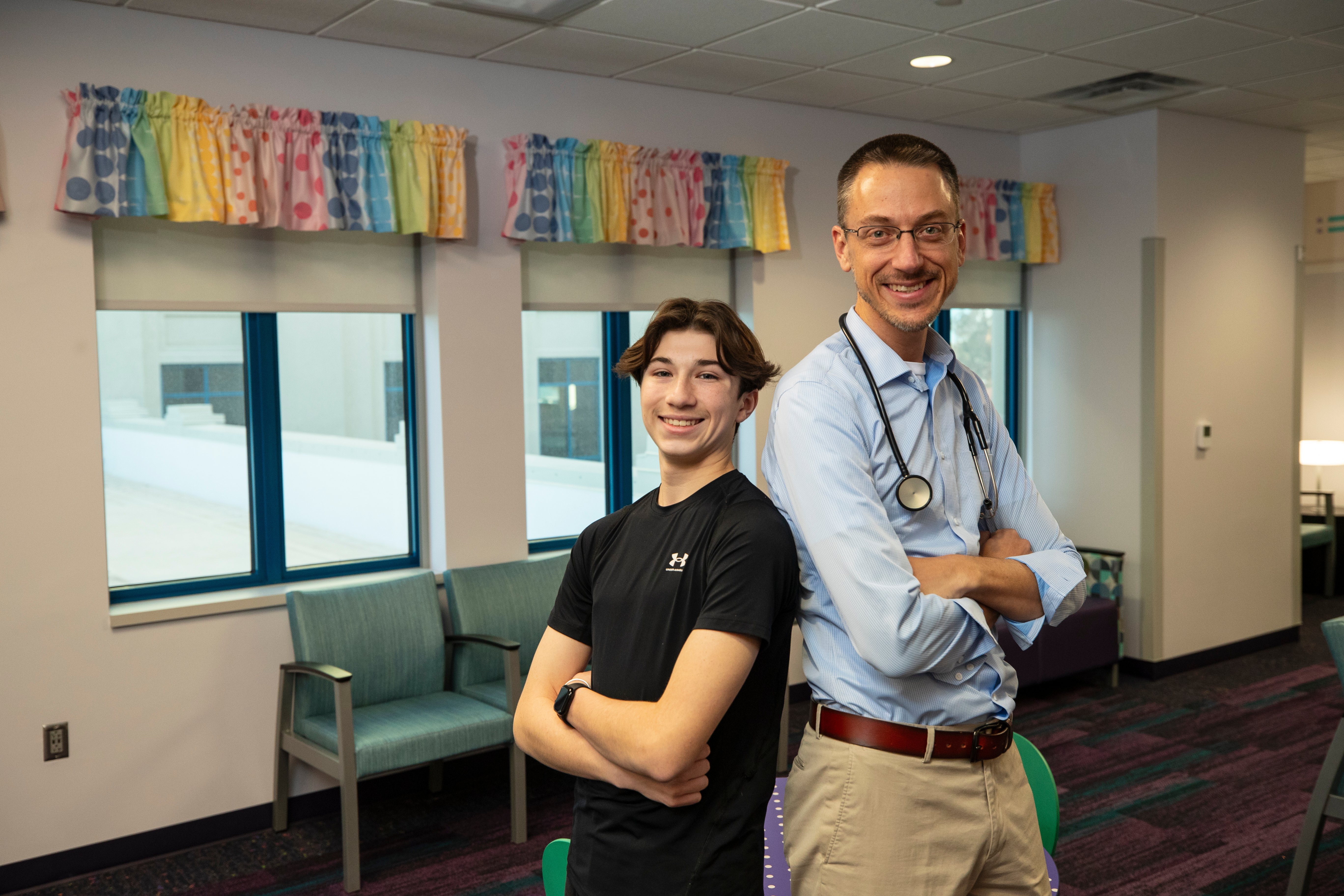 Doctor standing with patient in the lobby with arms crossed.